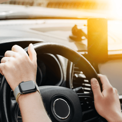 Business man hand on the steering wheel of a car that is blinded by bright sunlight in the windshield and man hand wear apple watch